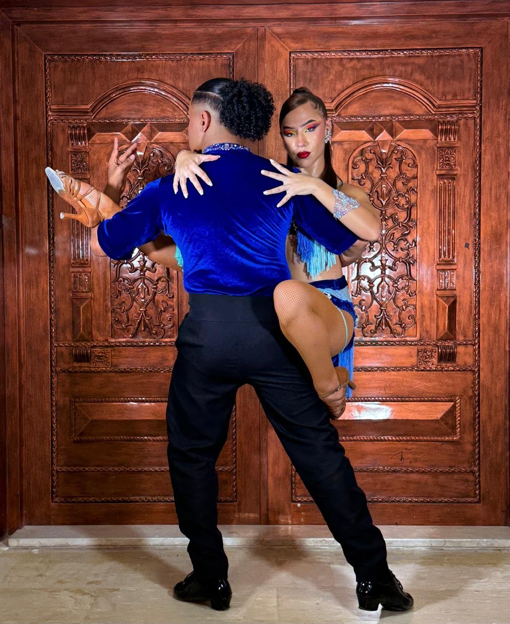 Salsa couple in royal blue mid-dip in front of carved wooden doors