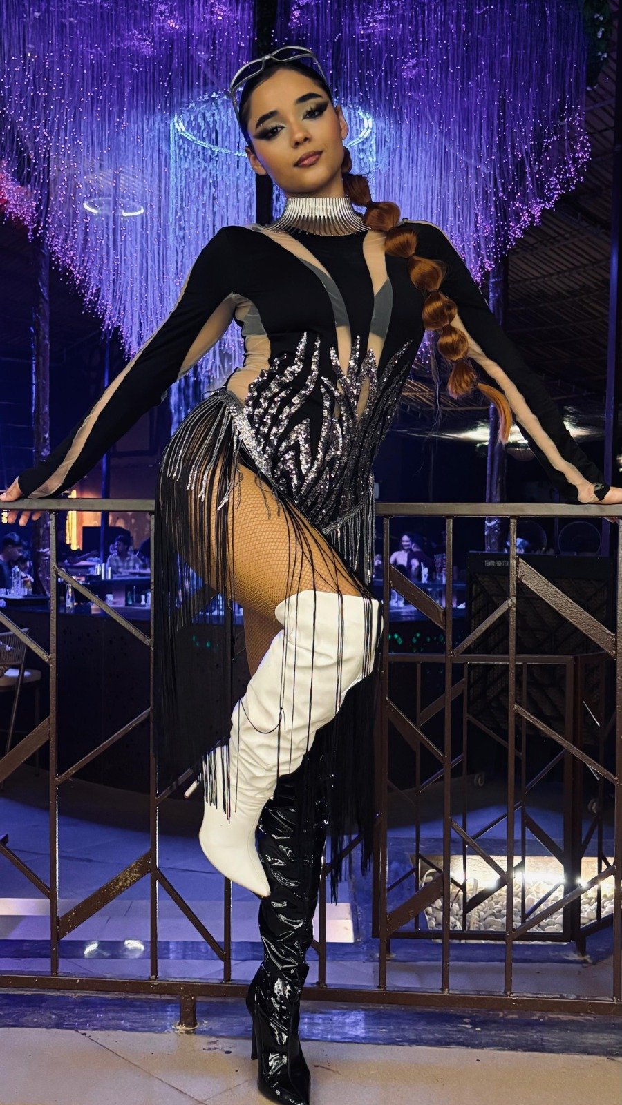Go-go dancer in a black fringed bodysuit and white boots under violet club lights